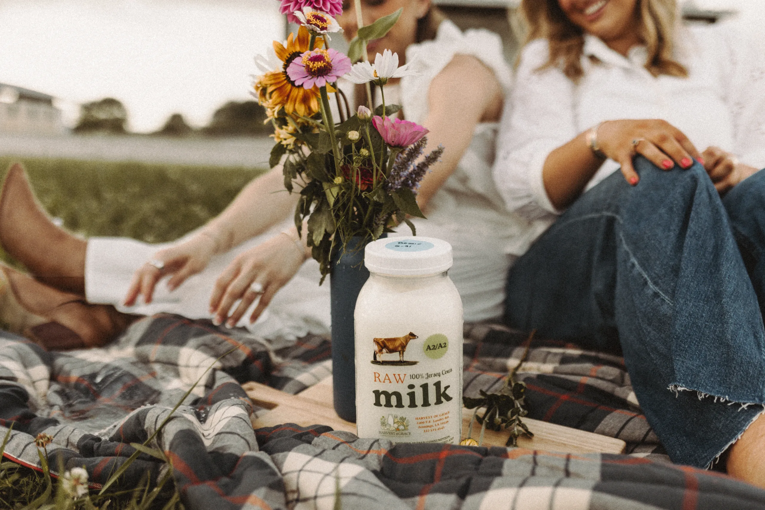 Jar of raw milk sits on a picnic blanket beside wildflowers and seated women. — louisiana web design case study
