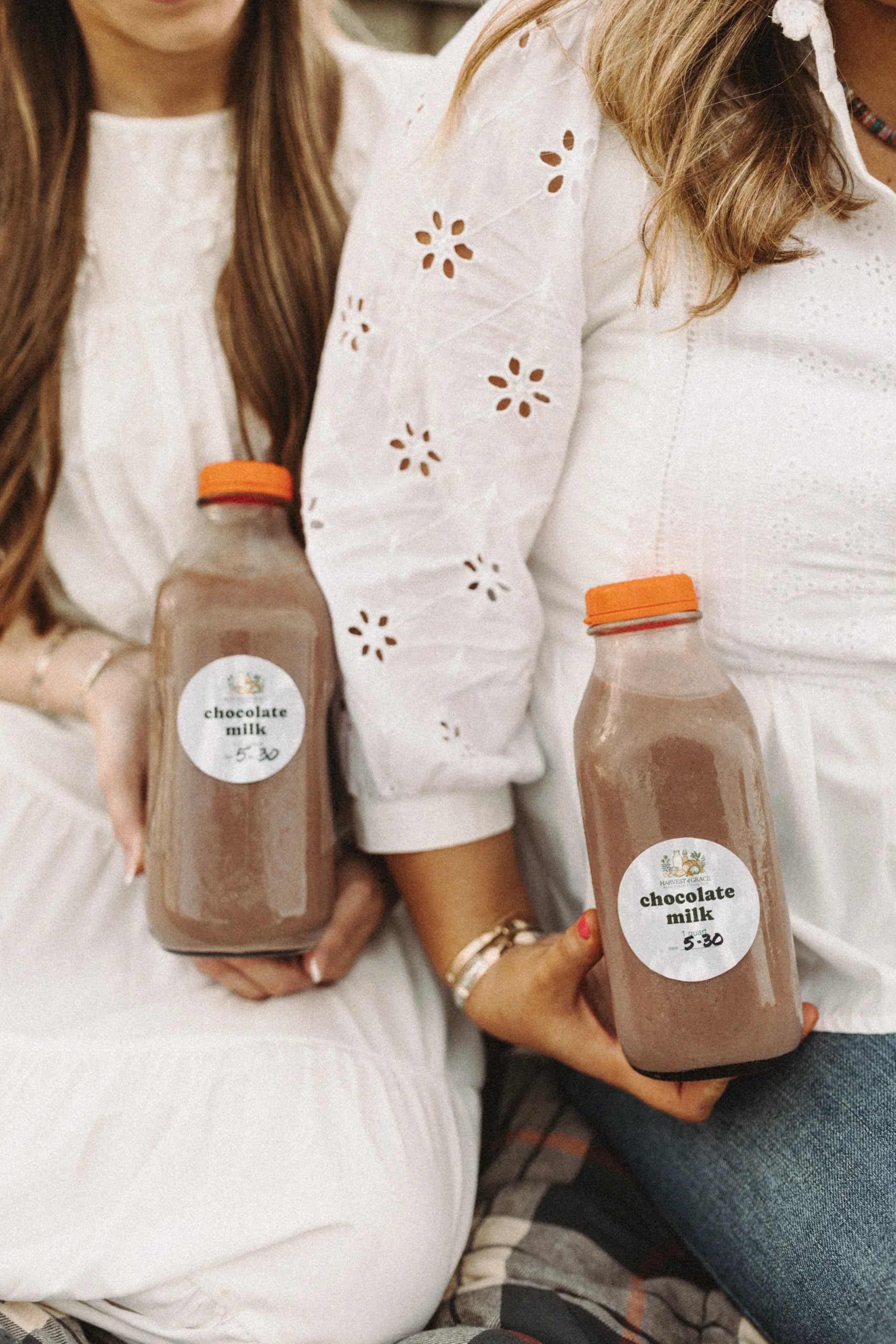 Two women in white hold bottles of chocolate milk with orange caps.