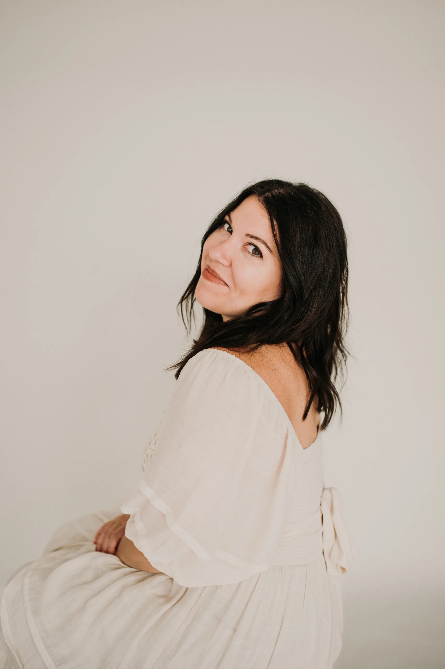 Woman in a white dress looking back over her shoulder against a plain background. — small business tools